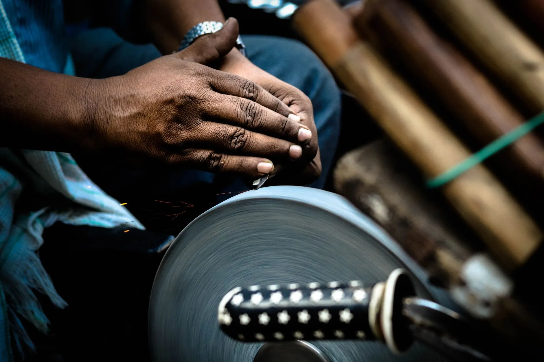 Hands sharpening a knife against a rotating grindstone in a market setting.