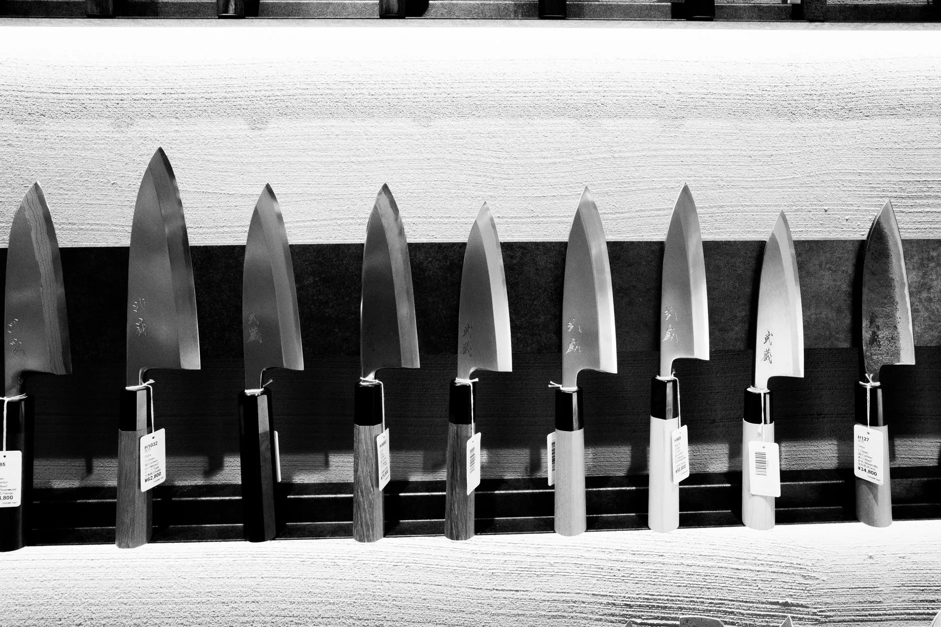 A striking black and white display of various Japanese chef's knives on a wooden holder.