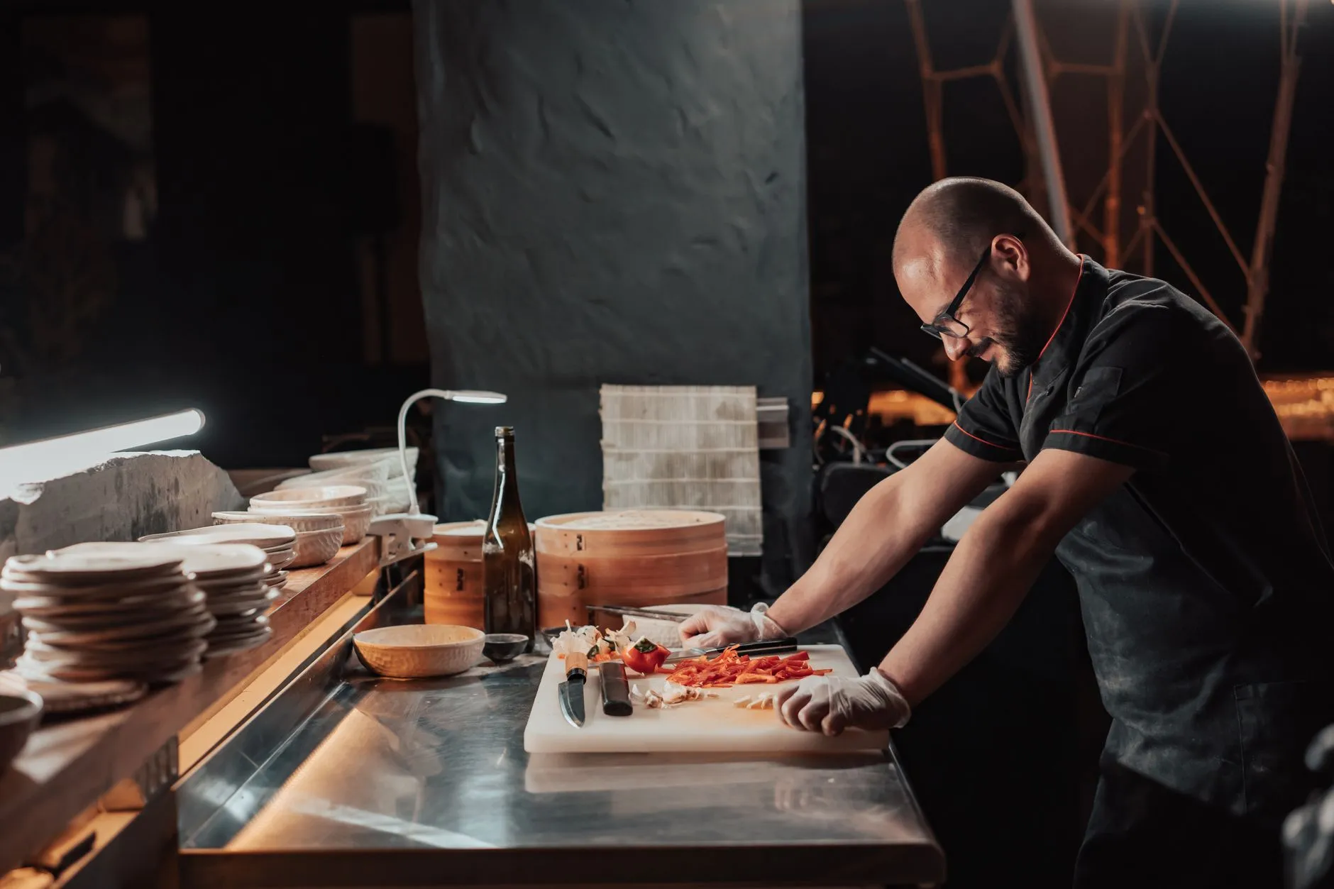 Chef slicing vegetables on a chopping board in a restaurant kitchen under ambient lighting.